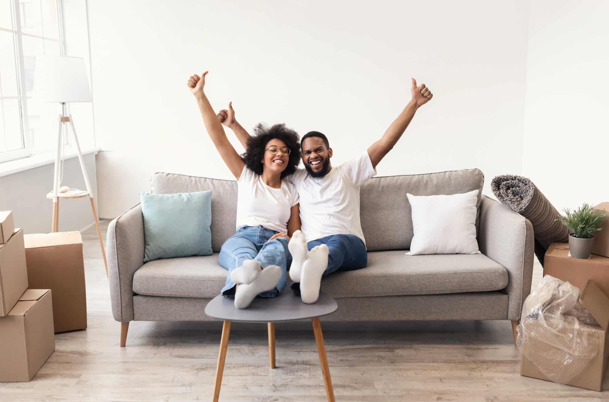 A couple sitting on a couch celebrating after being approved for a free heat pump through the Inflation Reduction Act.