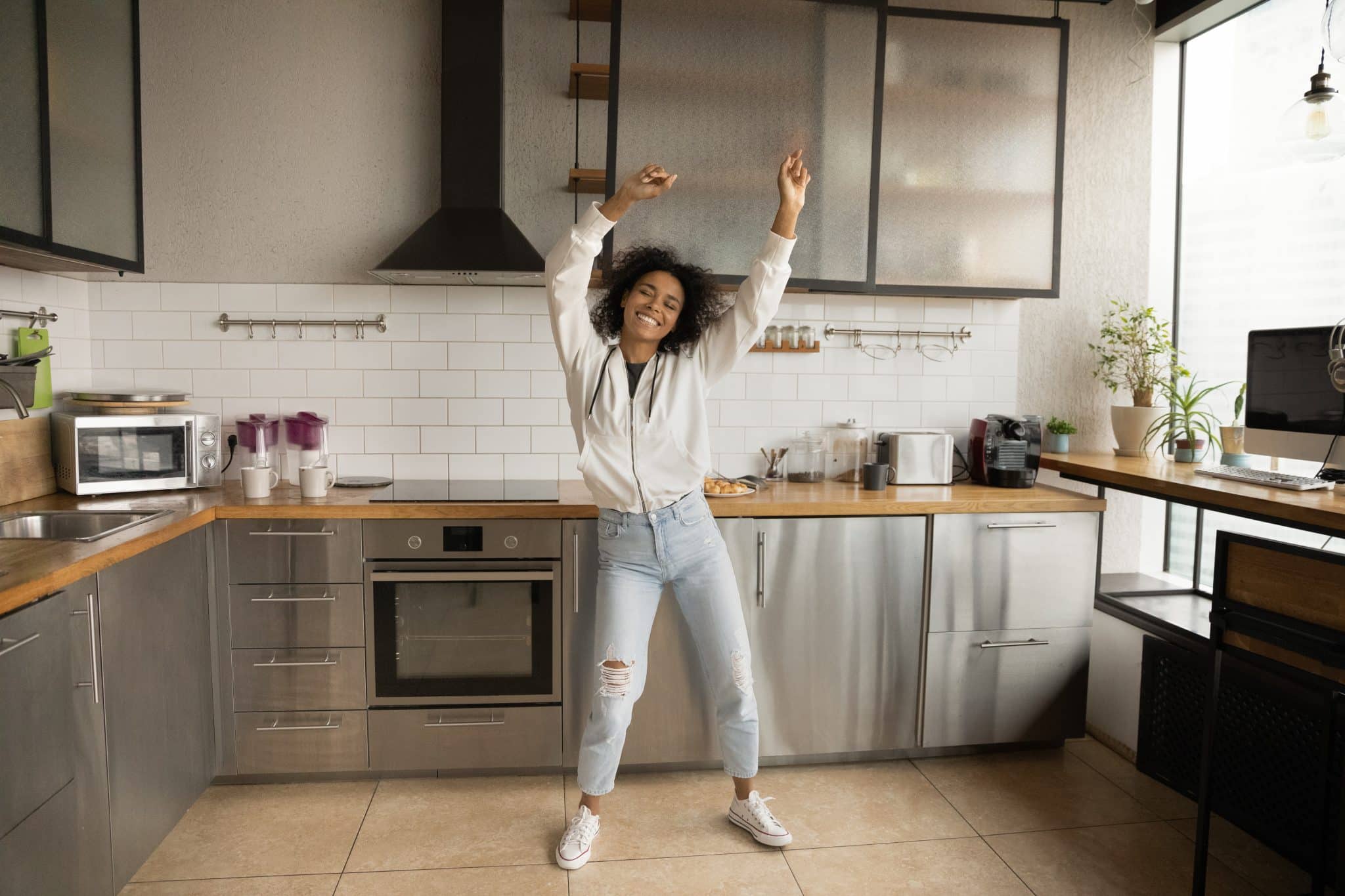 A cheerful woman dancing in her kitchen after receiving appliance rebates from the Inflation Reduction Act.