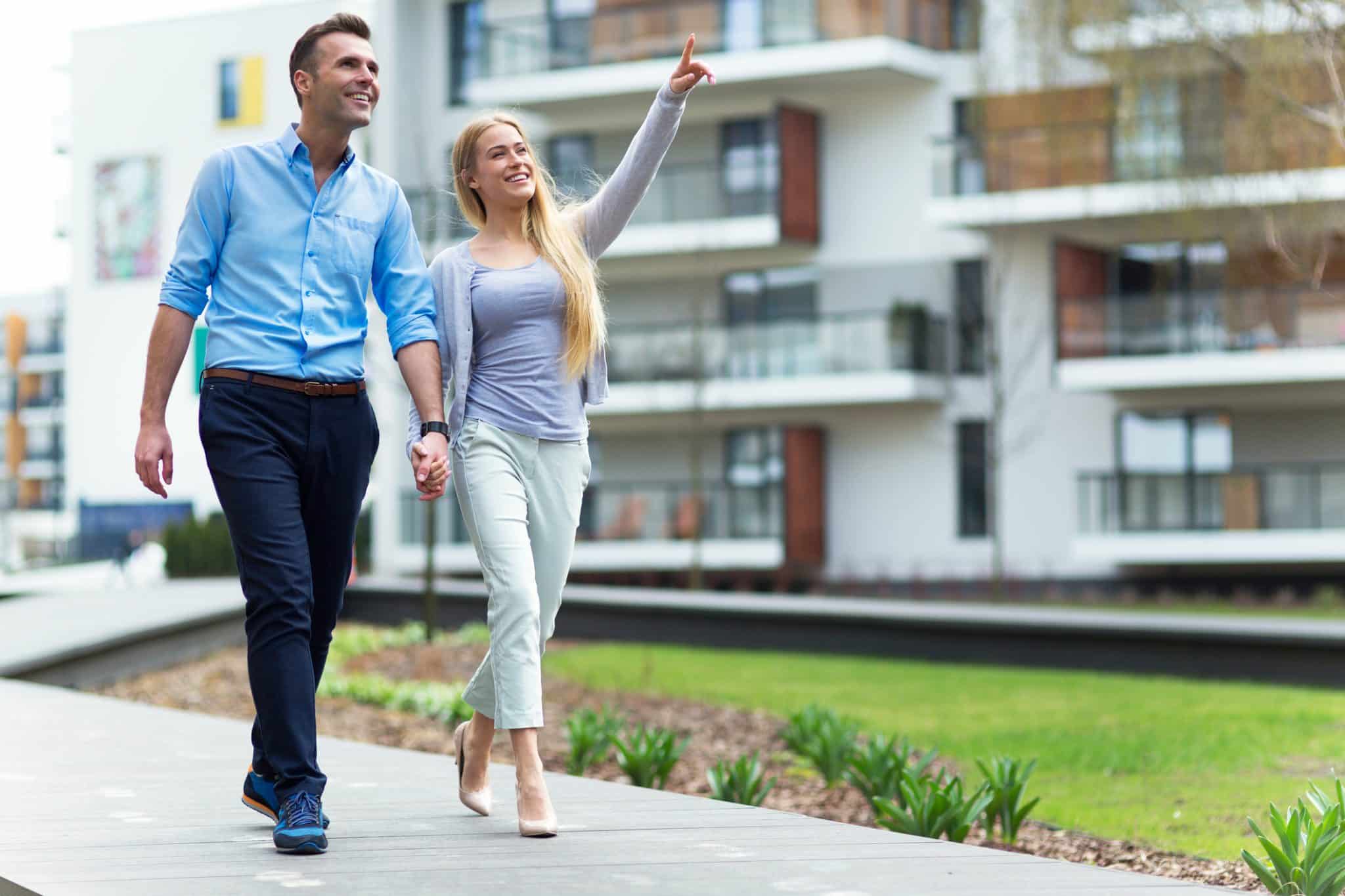 A man and woman holding hands while walking through the courtyard of an upgraded multi-family apartment complex.