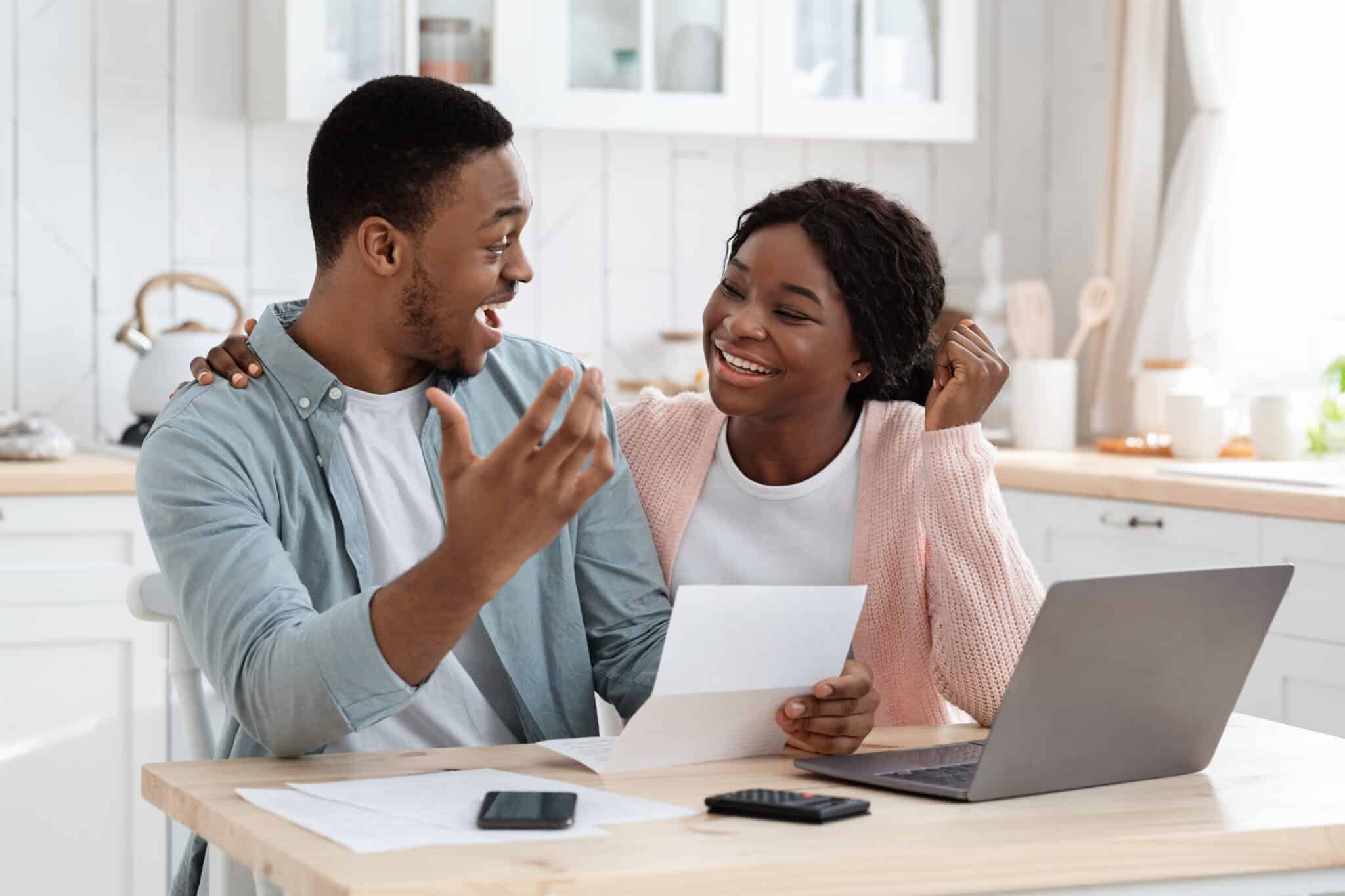 An excited couple sitting at their kitchen table smiling after receiving rebates from the Inflation Reduction Act.