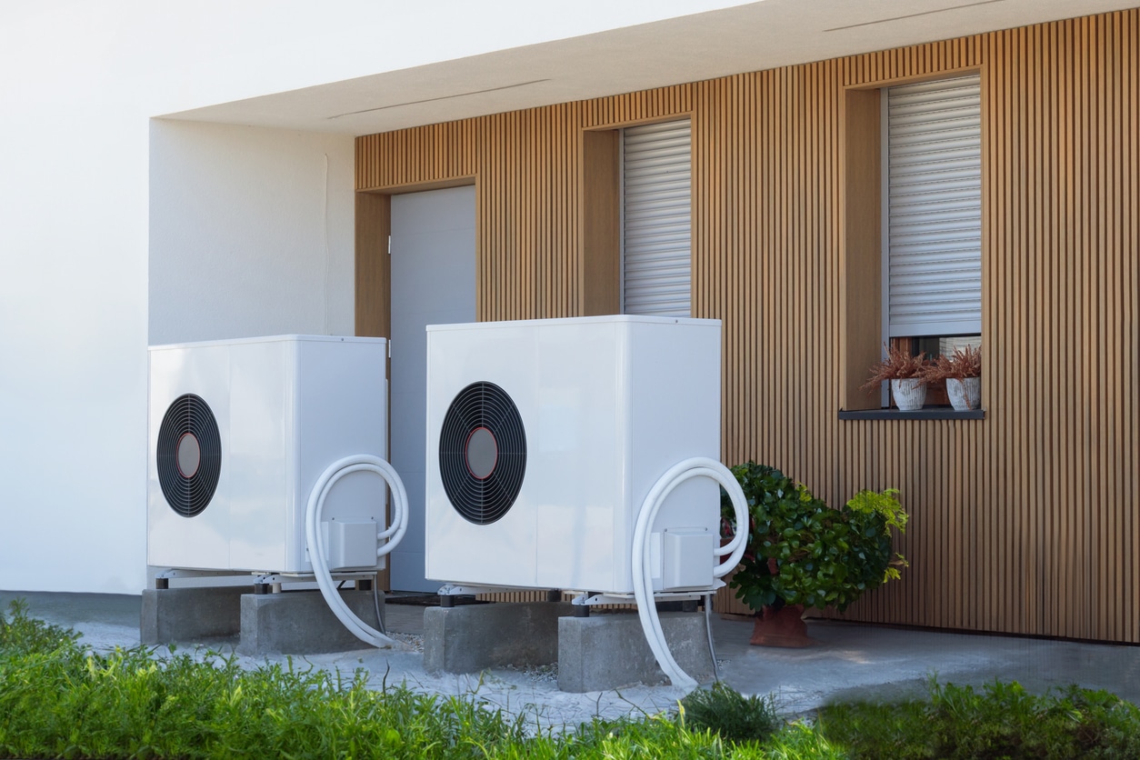 A professionally installed white heat pump outside of a modern home with a recessed patio area.